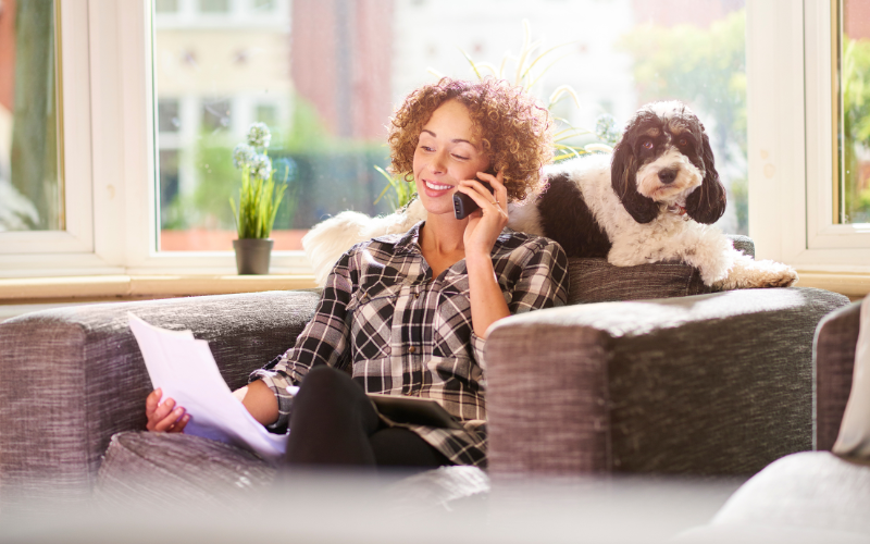 woman on phone while dog lays on couch behind her